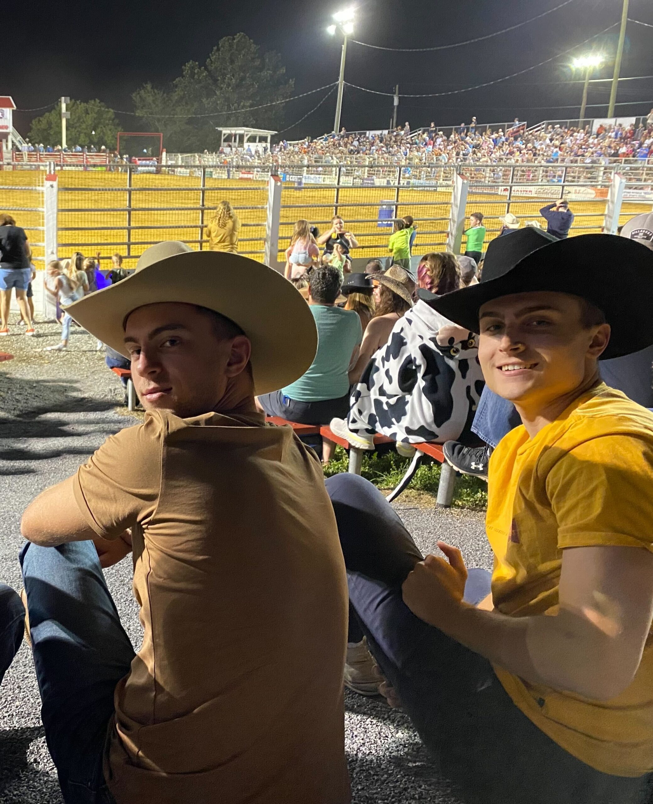 Jonathan and his friend sitting with cowboy hats at rodeo