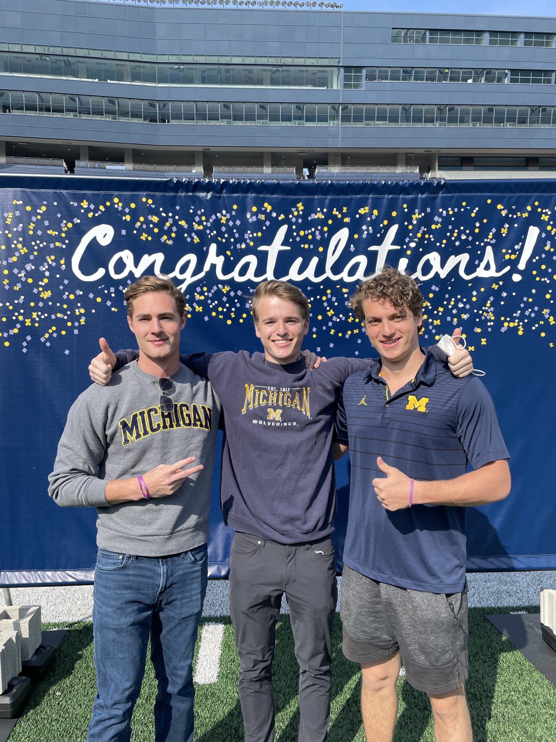 three Michigan students in front of congratulations banner